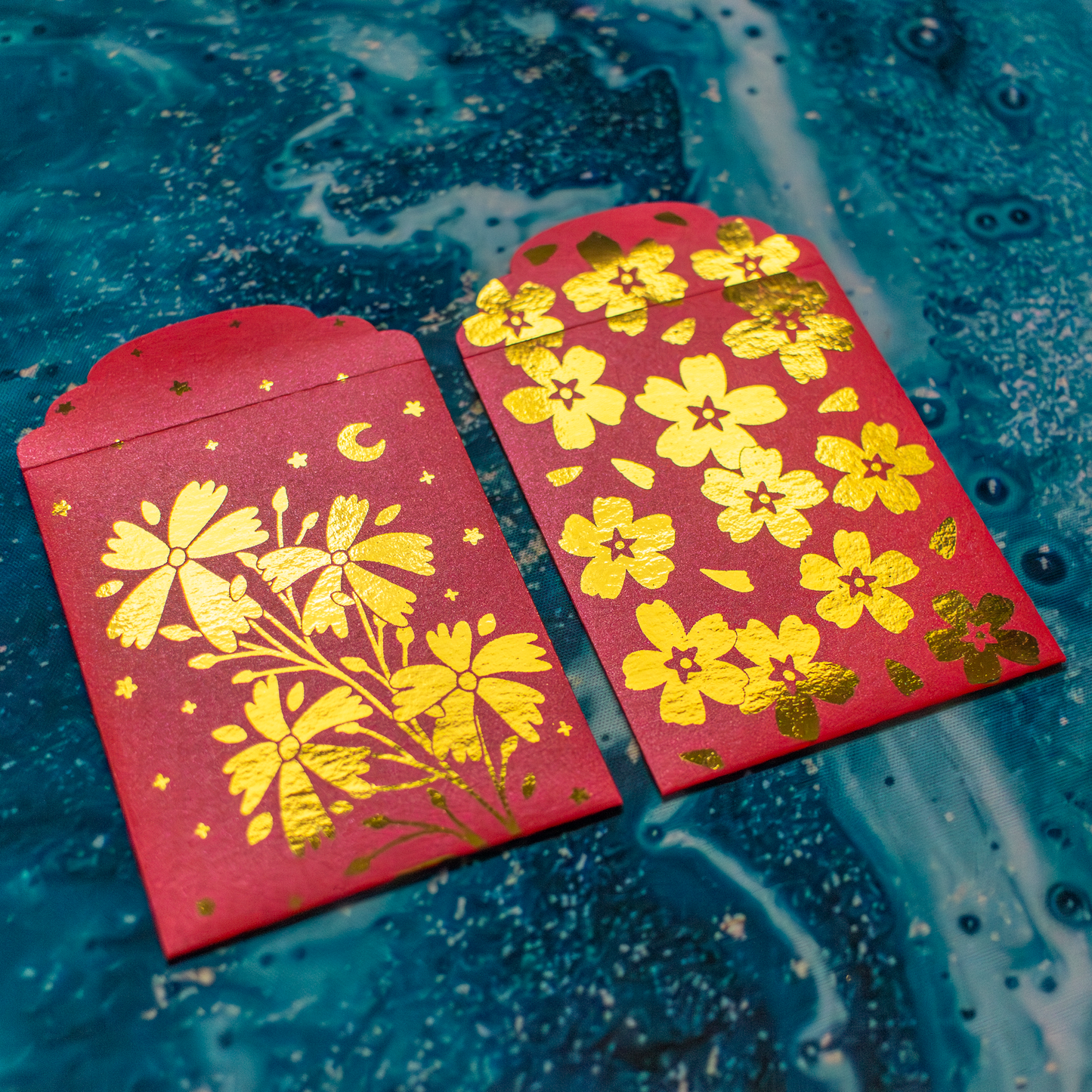 Two red envelopes with gold floral patterns on a blue textured background
