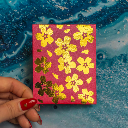 Red envelope with gold floral patterns held by a hand against a blue textured background